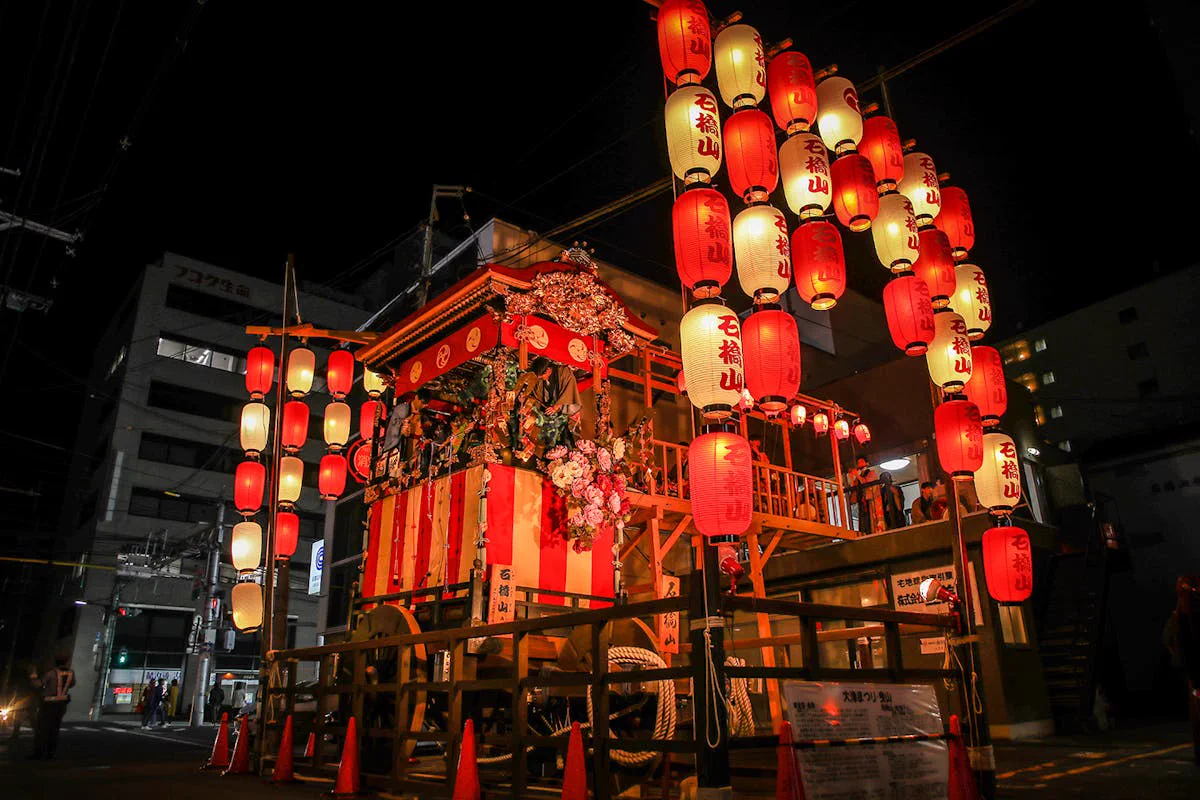 Vue nocturne de la rue entourée de nombreux lampions rouges et blancs autour du yama de l’Ōtsu Matsuri, nuit de la fête de la veille