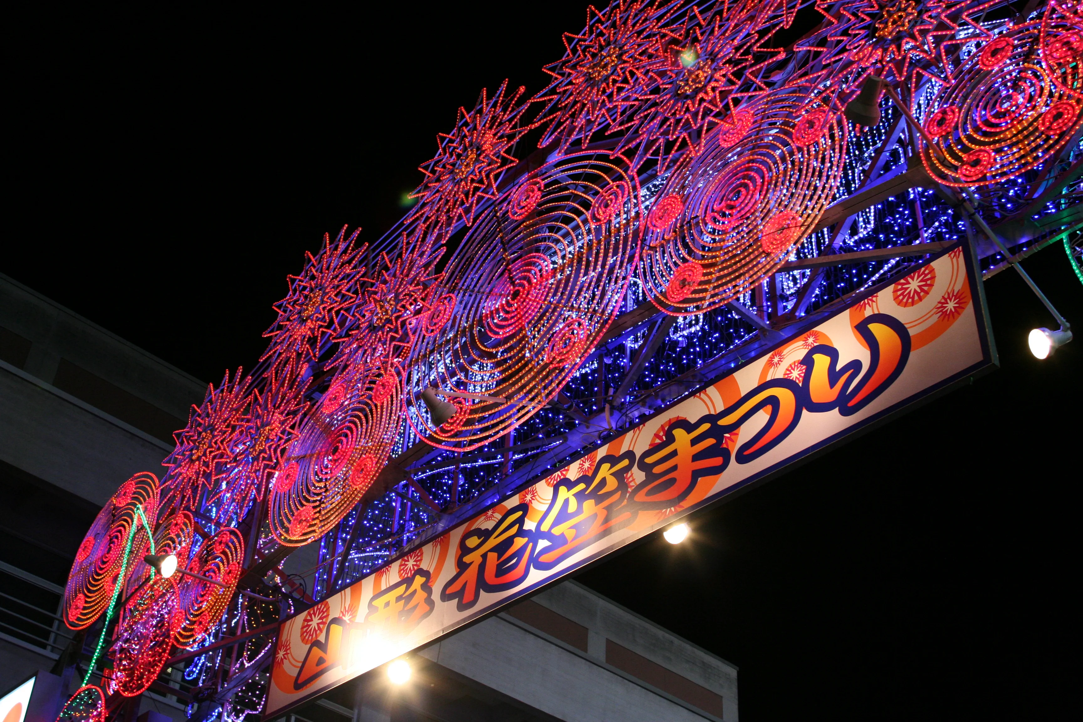 Danseurs du festival Hanagasa levant leurs chapeaux pendant le défilé nocturne, vu depuis la place payante et le parcours gratuit